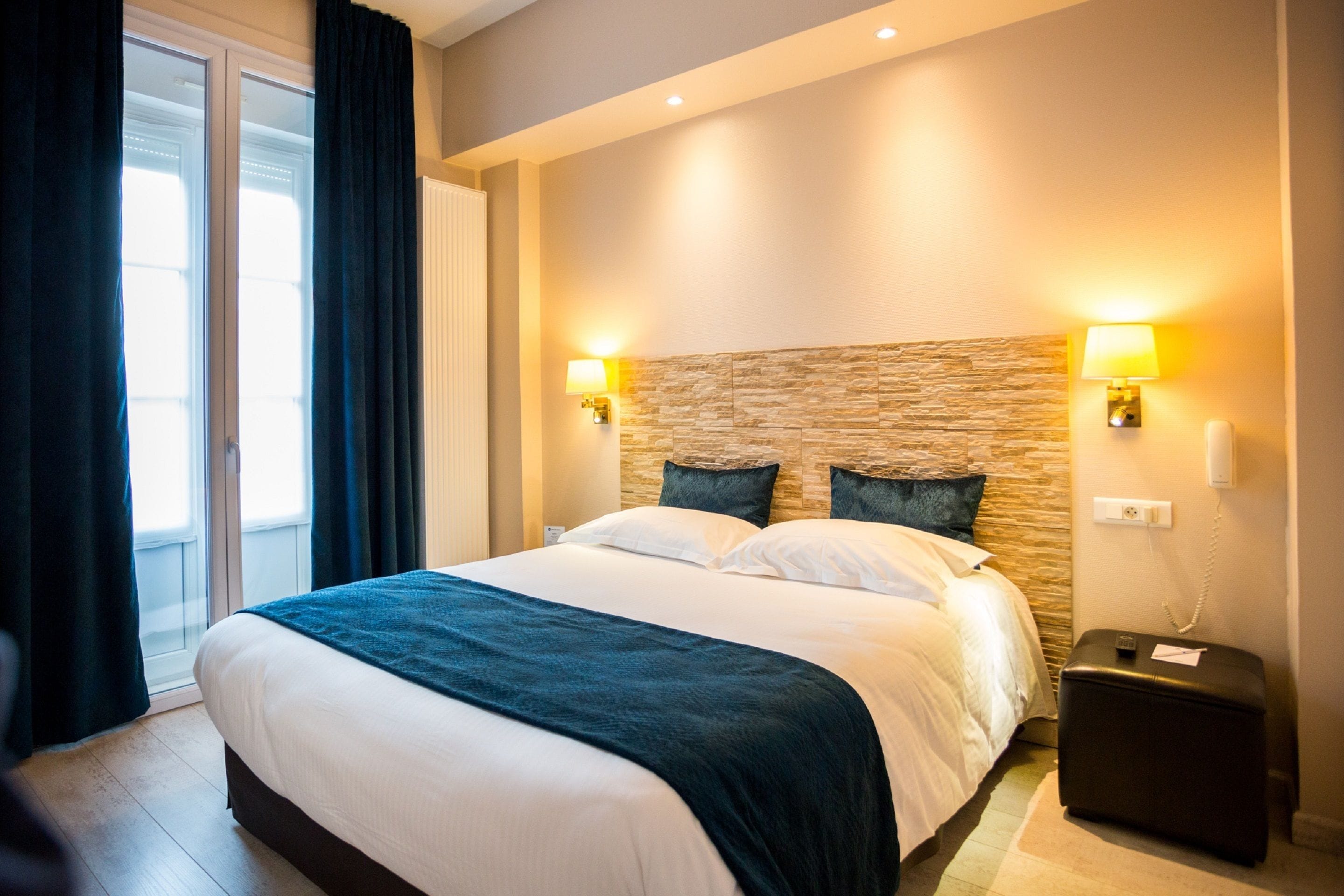 Una habitación de hotel con una cama grande, dos lámparas de noche, una pared decorativa de piedra, una mesita de noche y un teléfono.