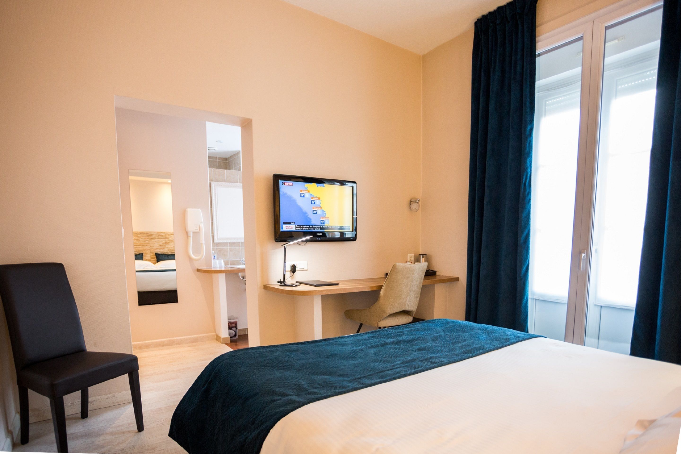 Une chambre d’hôtel avec un lit, un bureau équipé d’un ordinateur, une chaise et un téléviseur fixé au mur.
