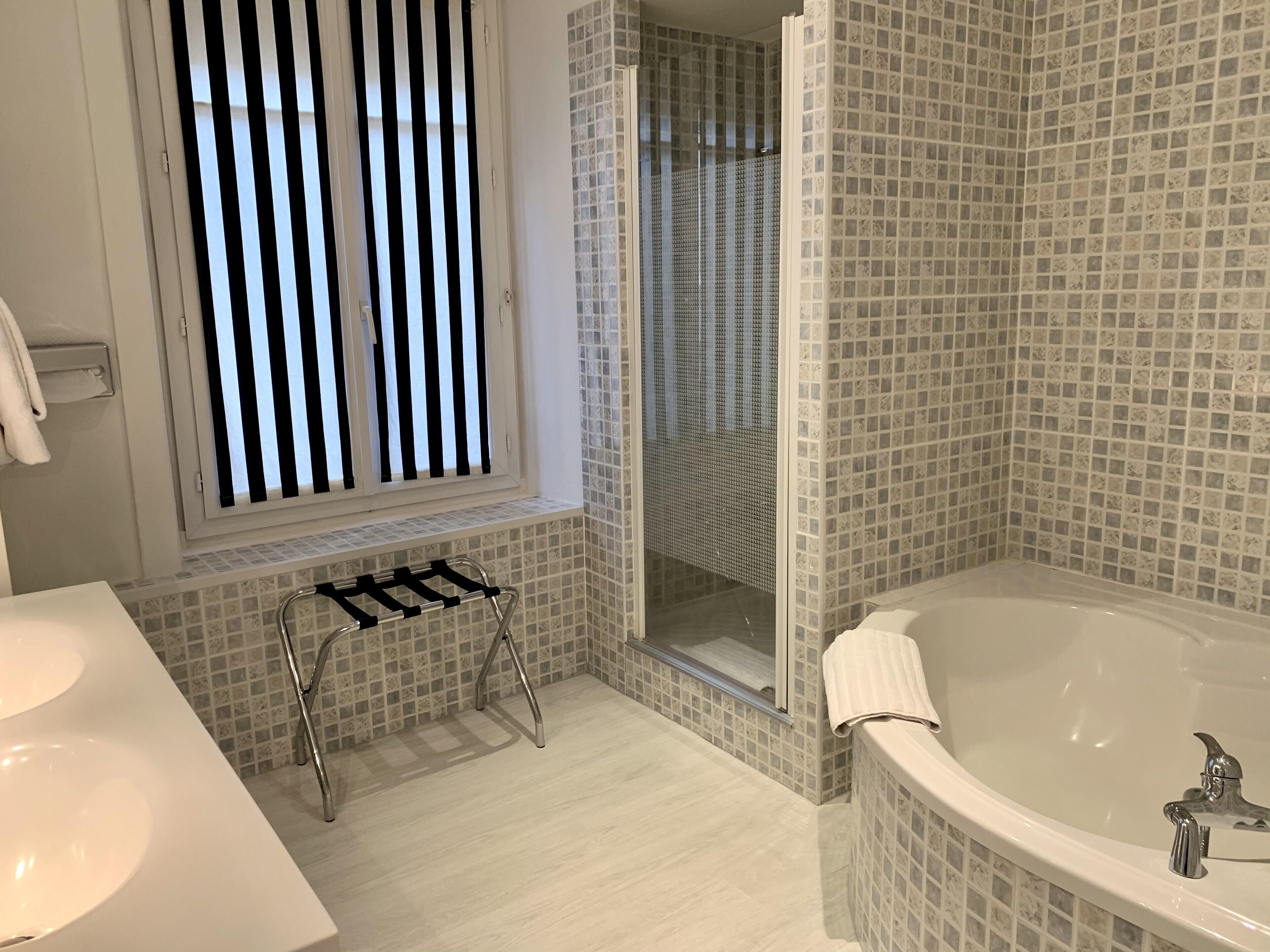A modern bathroom with a large bathtub, a window with vertical blinds, and a shower area.