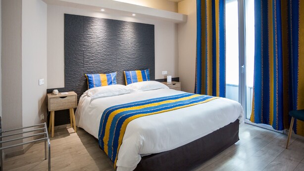 Ein modernes Hotelzimmer mit einem großen Bett, Holz-Nachttischen, einer Wand mit schwarzer Struktur und Blick ins Freie durch eine Schiebetür.