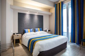 Ein modernes Hotelzimmer mit einem großen Bett, Holz-Nachttischen, einer Wand mit schwarzer Struktur und Blick ins Freie durch eine Schiebetür.