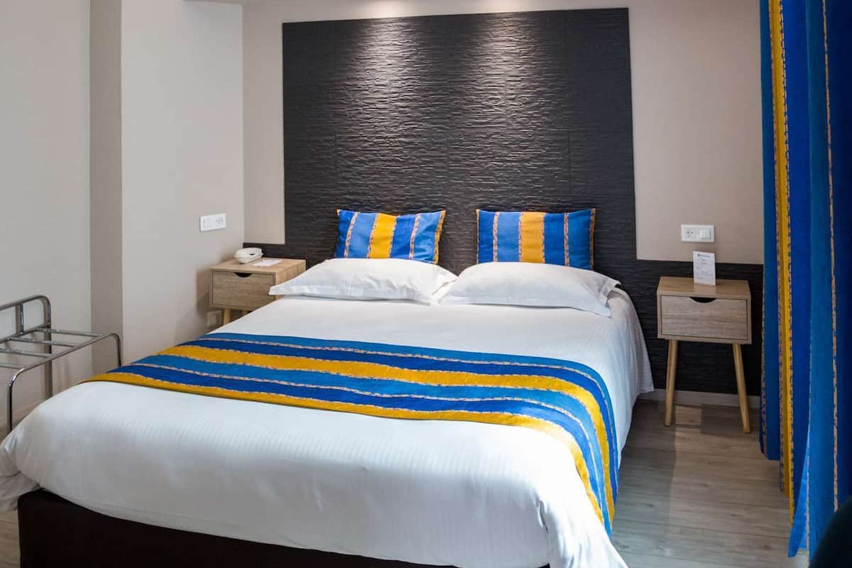 Una habitación de hotel moderna con una cama grande, mesitas de noche y cabecero.