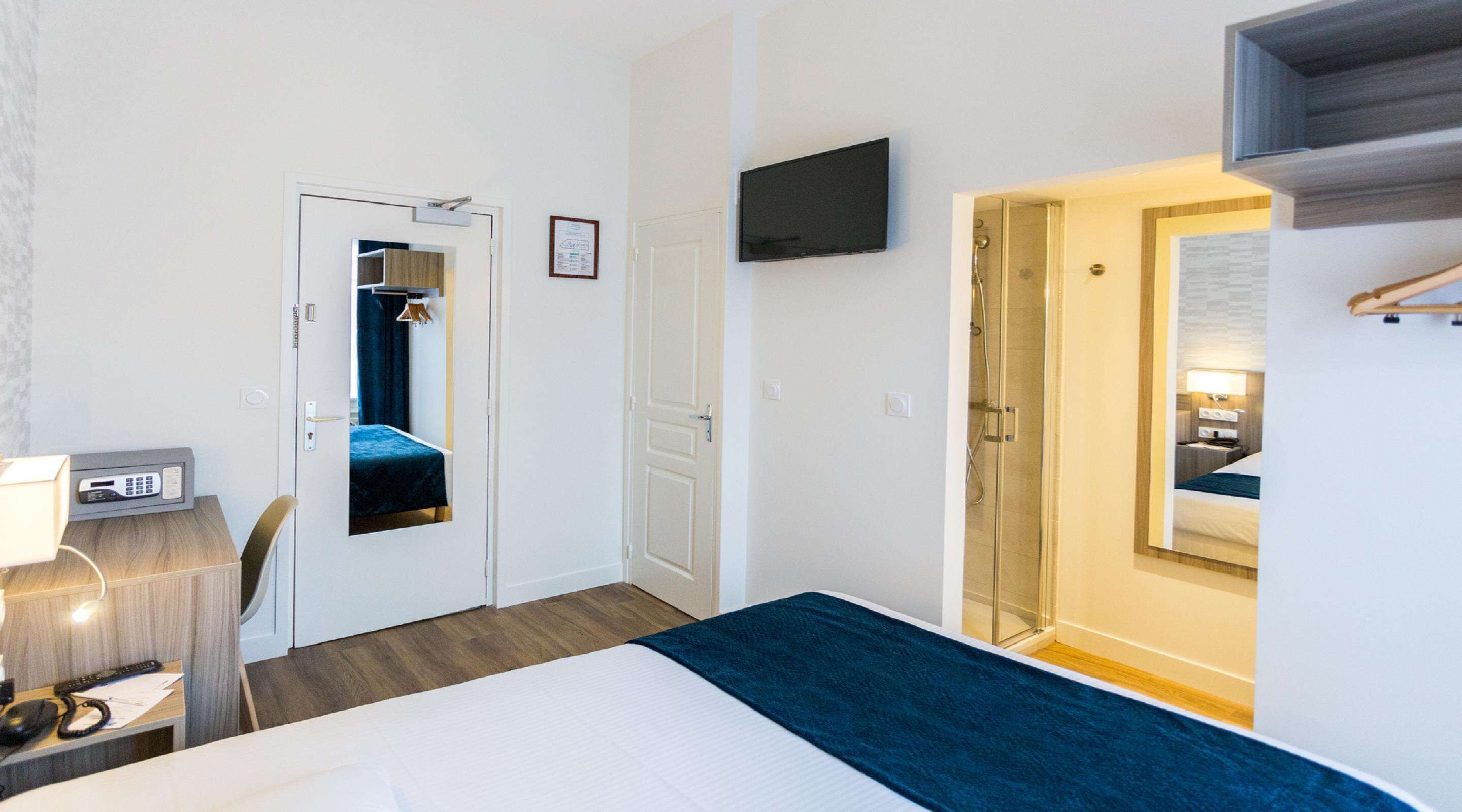 Une chambre d’hôtel comprenant un lit, un bureau avec un téléphone, un téléviseur fixé au mur et un espace douche.