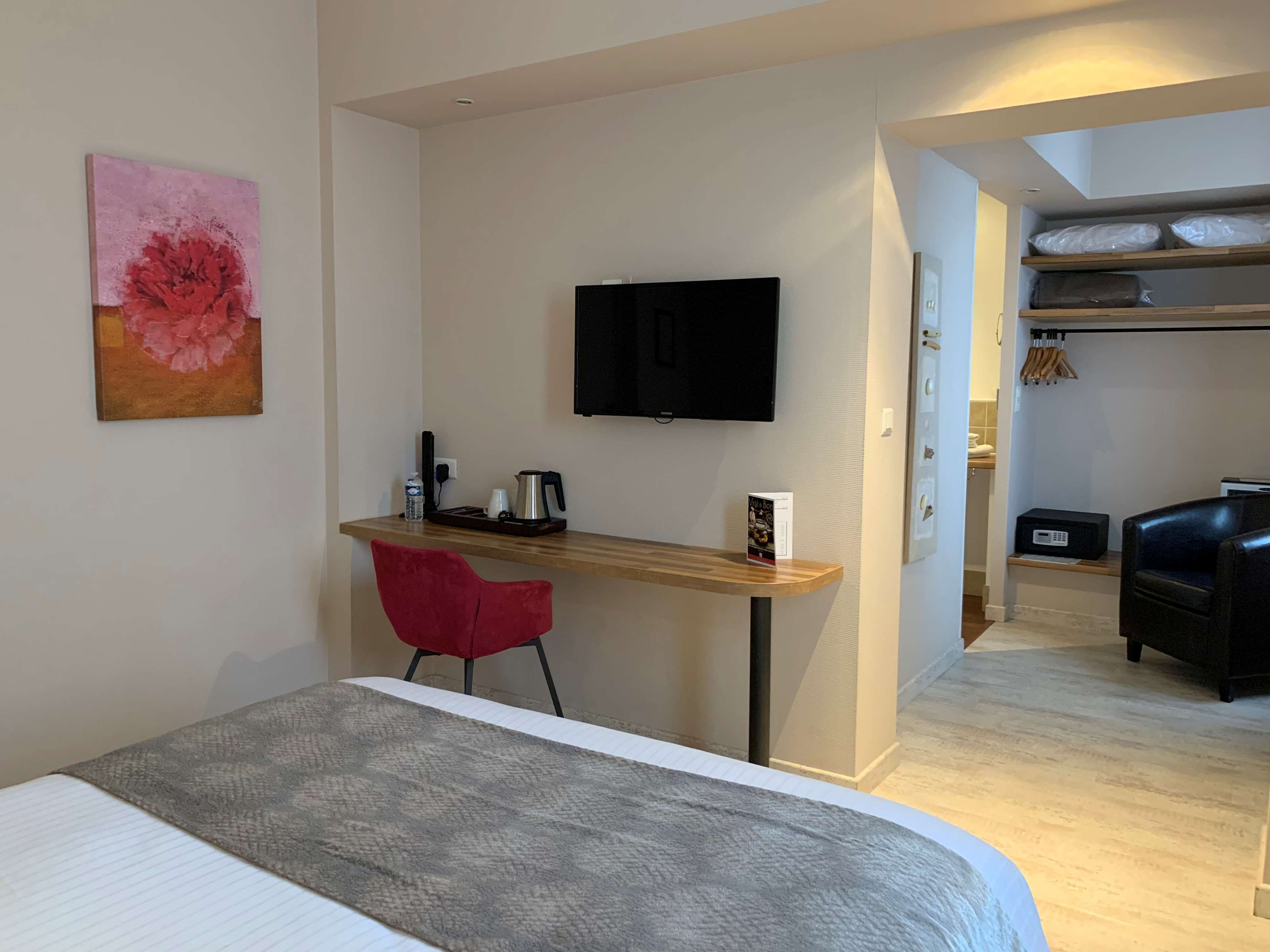 Ett hotellrum med en säng, ett skrivbord med en stol, en tv och en tavla på väggen.