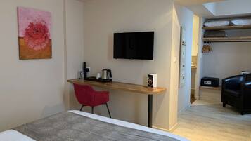 Ett hotellrum med en säng, ett skrivbord med en stol, en tv och en tavla på väggen.