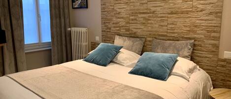 Un dormitorio con una cama grande, un cabecero con diseño de piedra, un radiador y una pequeña mesa redonda.
