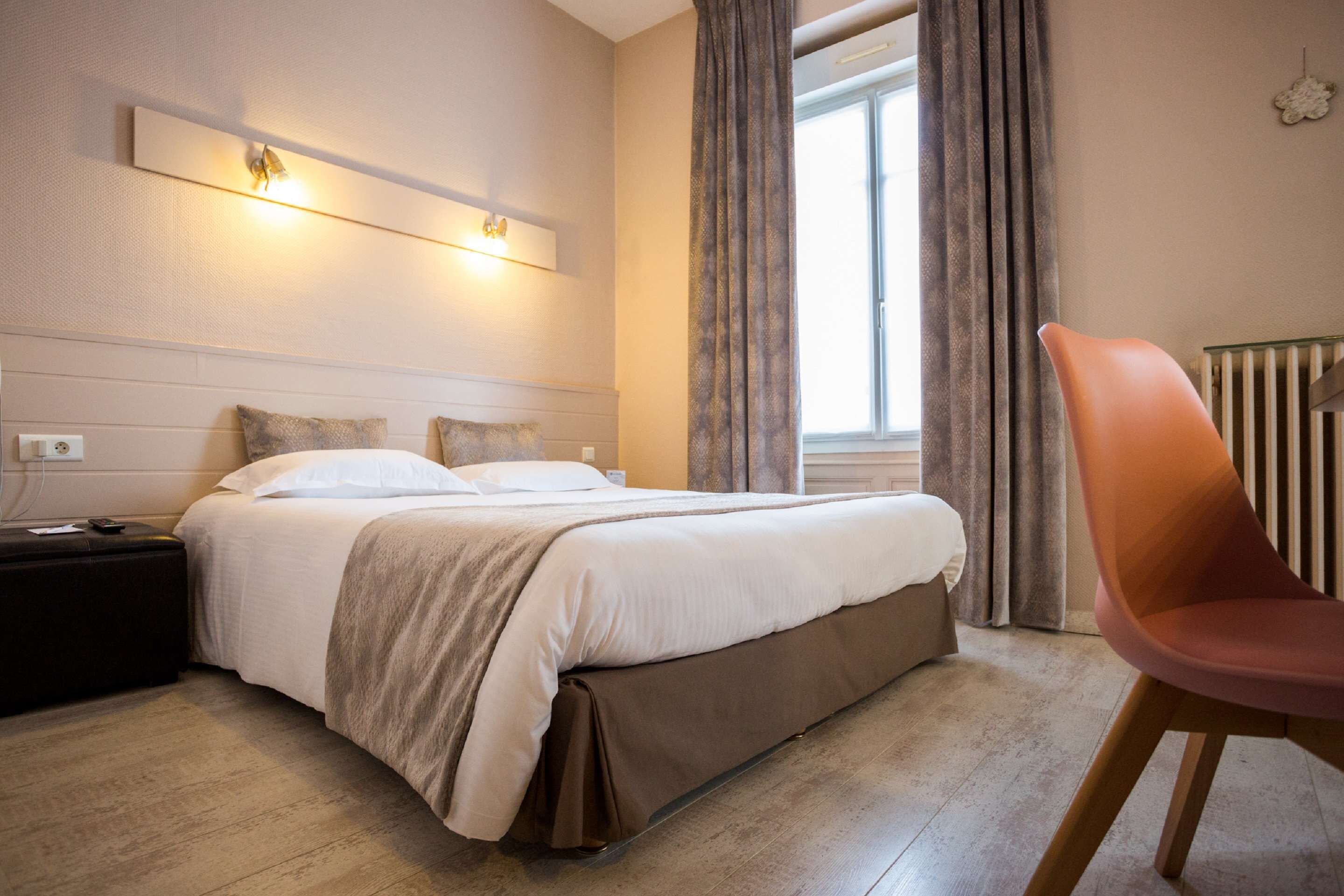 A hotel room with a bed, a nightstand, a chair, and a window with curtains.