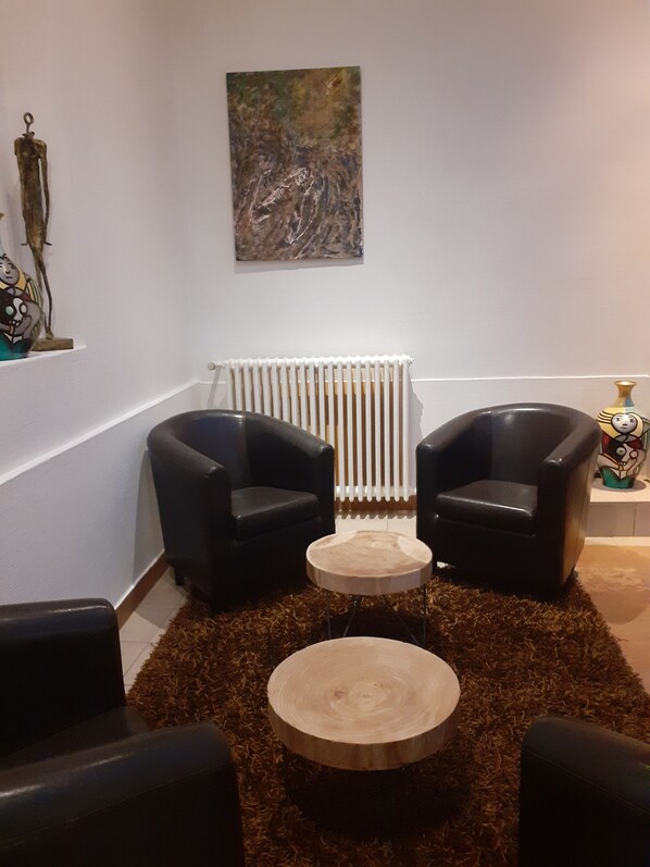 A modern living room with two black leather armchairs, a round wooden coffee table, a radiator, and a painting on the wall.