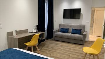 Moderni hotellihuone, jossa on sänky, työpöytä tuolilla, sohva koristetyynyillä ja seinälle asennettu televisio.