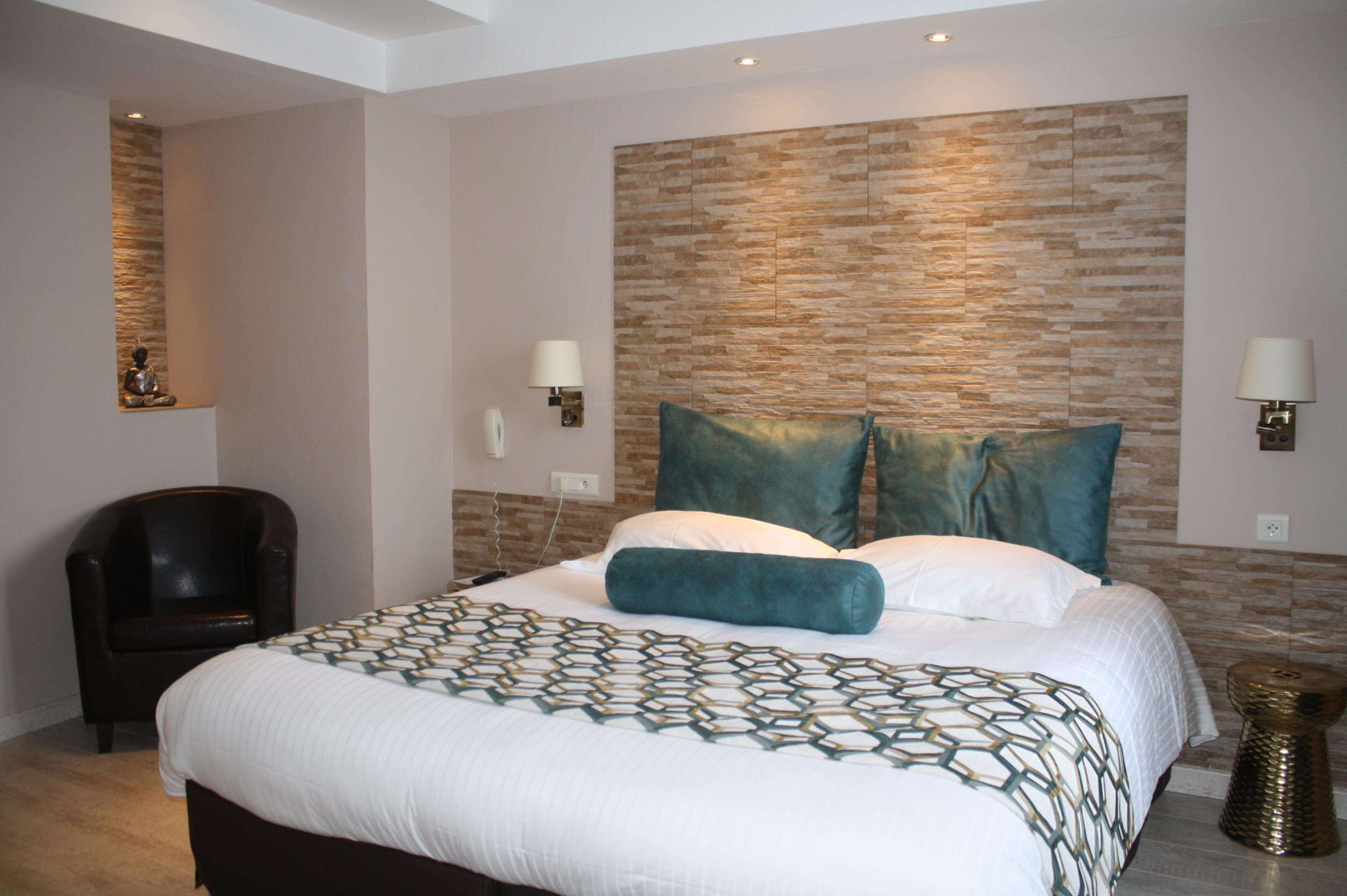 A hotel room with a large bed, a chair, a wall-mounted lamp, and a decorative wall panel.