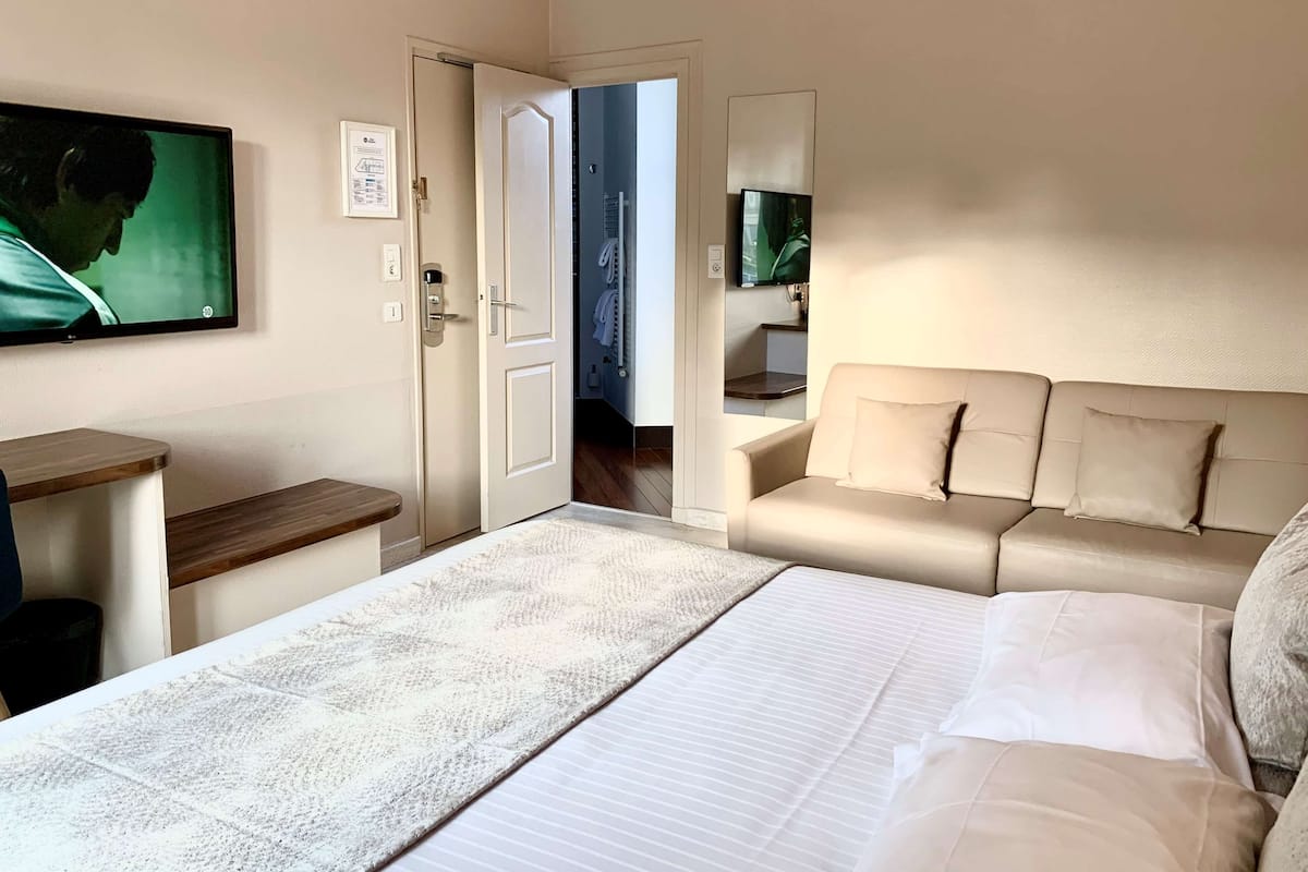 Una habitación de hotel con cama, sofá, televisor y puerta que da a un baño.