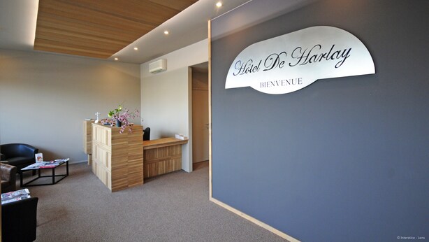 A reception area with a wooden desk, a reception desk, and a wall-mounted sign that reads "Hotel De Harlay." - Citotel De Harlay (Compiègne)