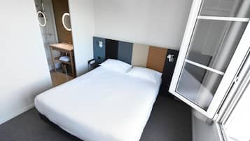 Una habitación de hotel con cama, un baño pequeño con espejo y una ventana.