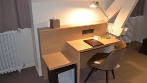 Une chambre compacte comprenant un lit simple, un bureau avec une chaise, un radiateur et un petit meuble de rangement.