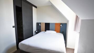 A modern hotel room with a large bed, a wardrobe, a desk with a lamp, and a view of the sky.