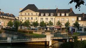 A riverside view with a bridge, buildings, and trees. - Citotel De Harlay (Compiègne)