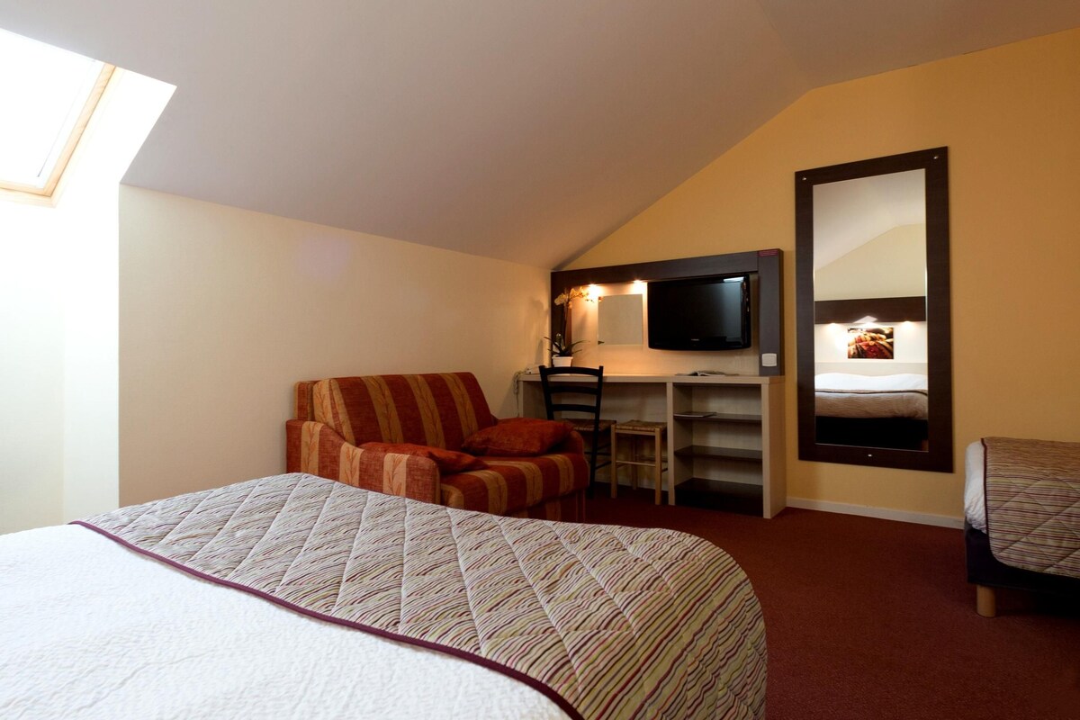 A bedroom with a bed, a desk, a chair, a TV, and a mirror.