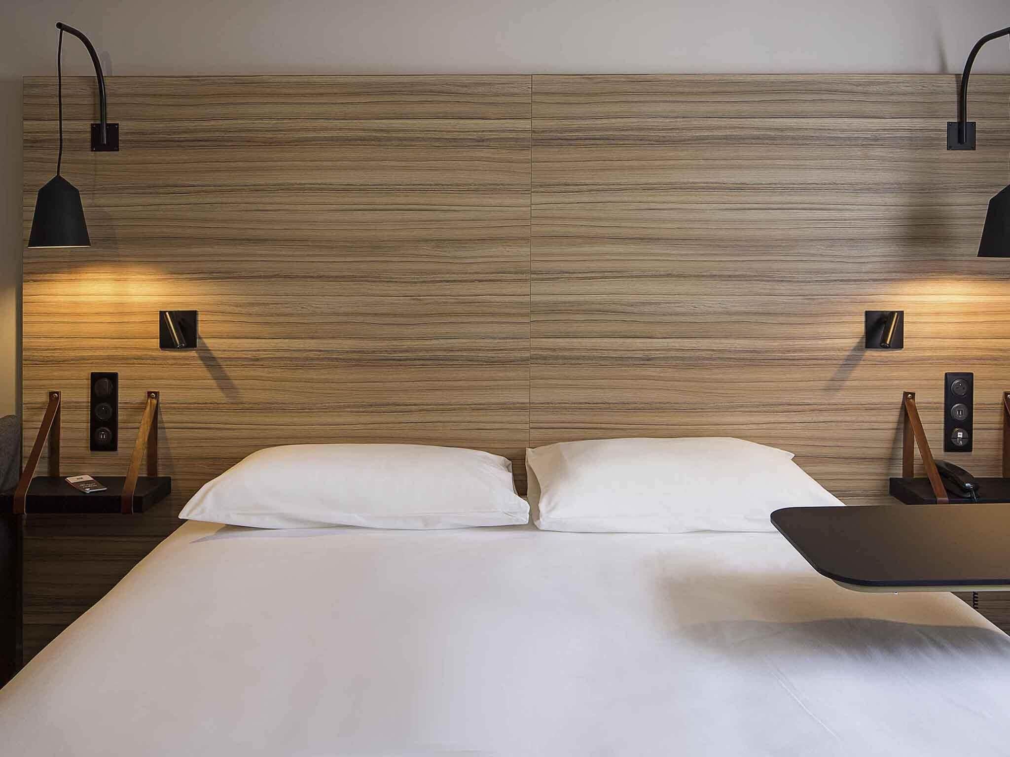 A double bed with a wooden headboard, two bedside tables with lamps, and a small nightstand with a phone.