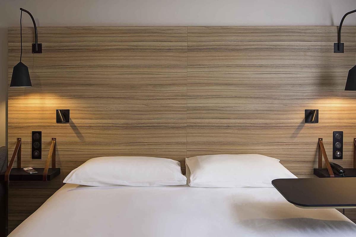 A double bed with a wooden headboard, two bedside tables with lamps, and a small nightstand with a phone.