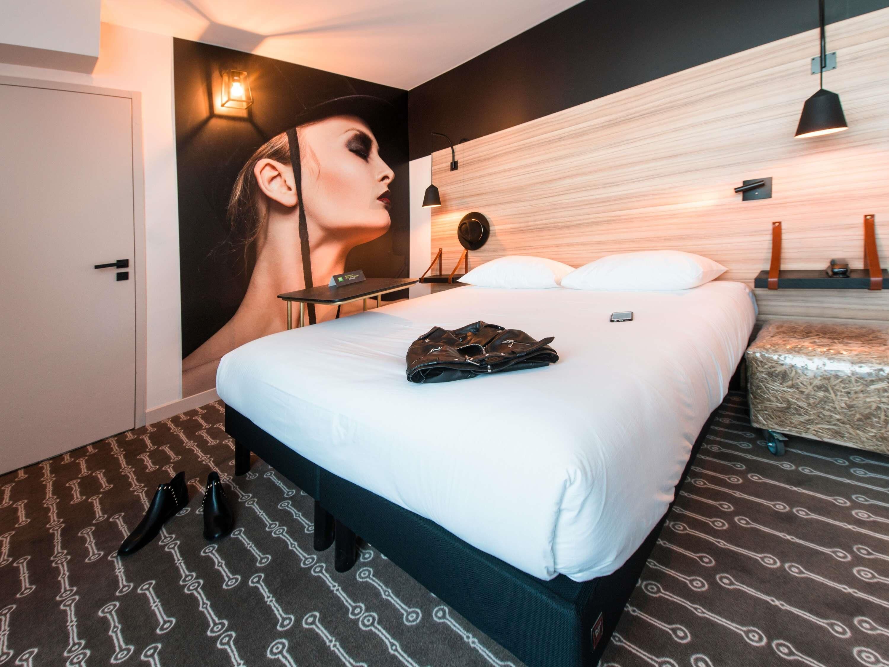 Une chambre d’hôtel avec un grand lit, une table de chevet, une lampe fixée au mur et une affiche accrochée au mur.