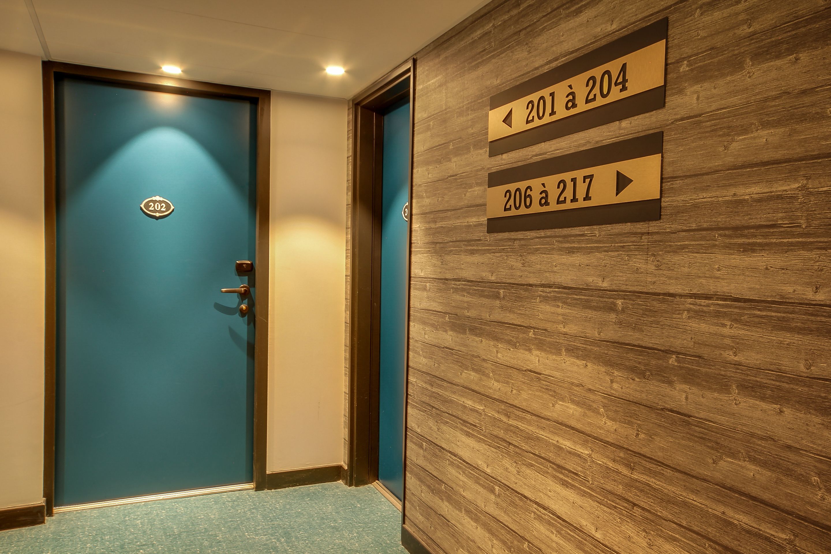 A hotel corridor with a blue door labeled 202, and directional signs indicating room numbers 201 to 204 and 206 to 217.