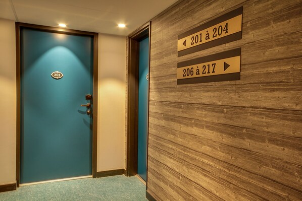 A hotel corridor with a blue door labeled 202, and directional signs indicating room numbers 201 to 204 and 206 to 217.