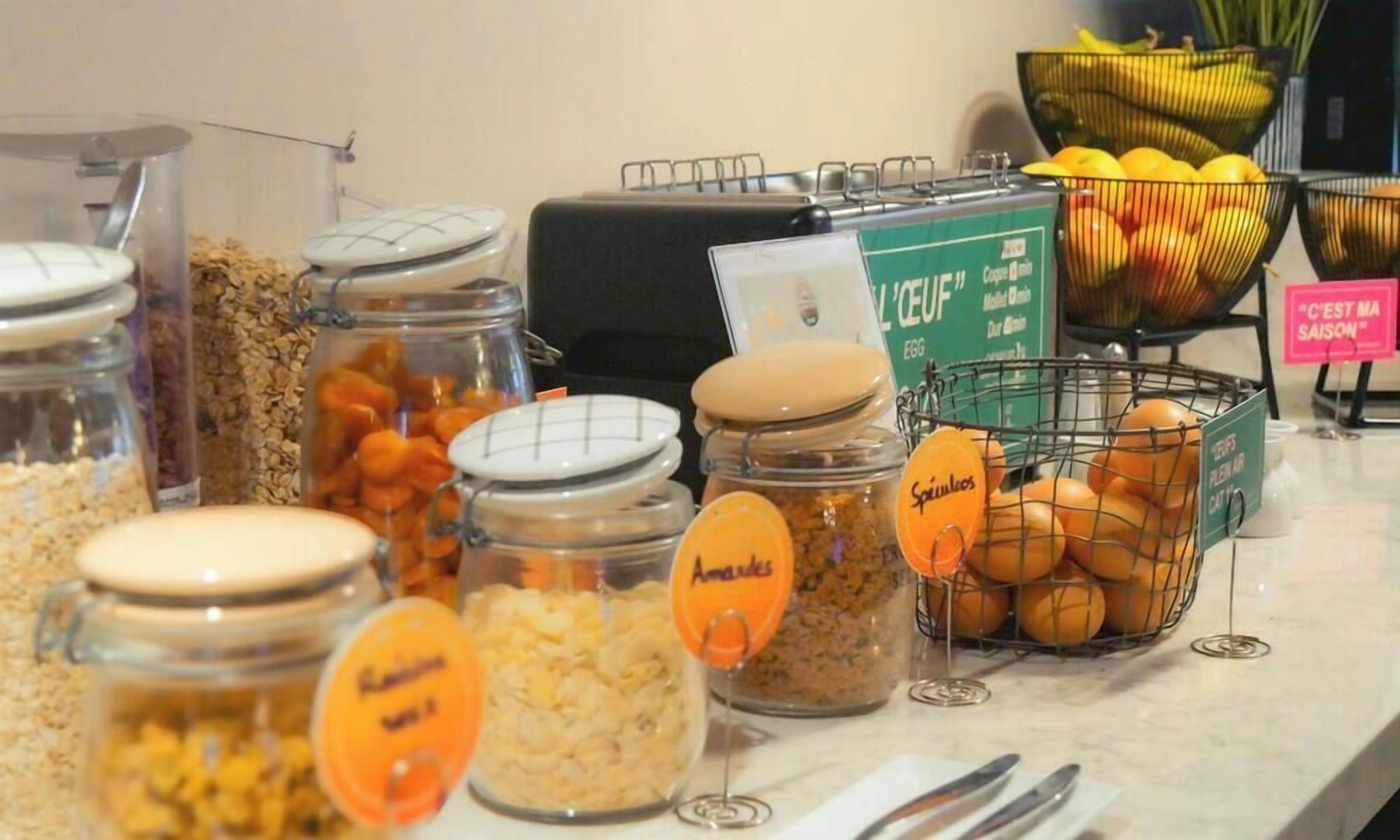 A buffet area with various food items in glass containers and baskets, including cereals, snacks, and fruits.