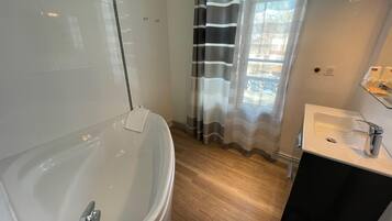 Ett modernt badrum med ett fristående badkar, en dusch med glasväggar och en tvättställsmöbel med handfat och spegel.