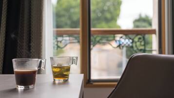 Una mesa con dos vasos de bebidas, una ventana que da a zonas verdes y una silla.