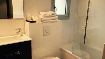 Un baño moderno con un lavamanos, inodoro y bañera blancos. Hay una ventana sobre el inodoro, y una toalla doblada sobre la bañera.