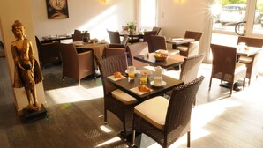 A dining area with wicker chairs, tables set with breakfast items, a Buddha statue, and a Buddha painting on the wall. - Hôtel du Moulin, Niort (Niort)