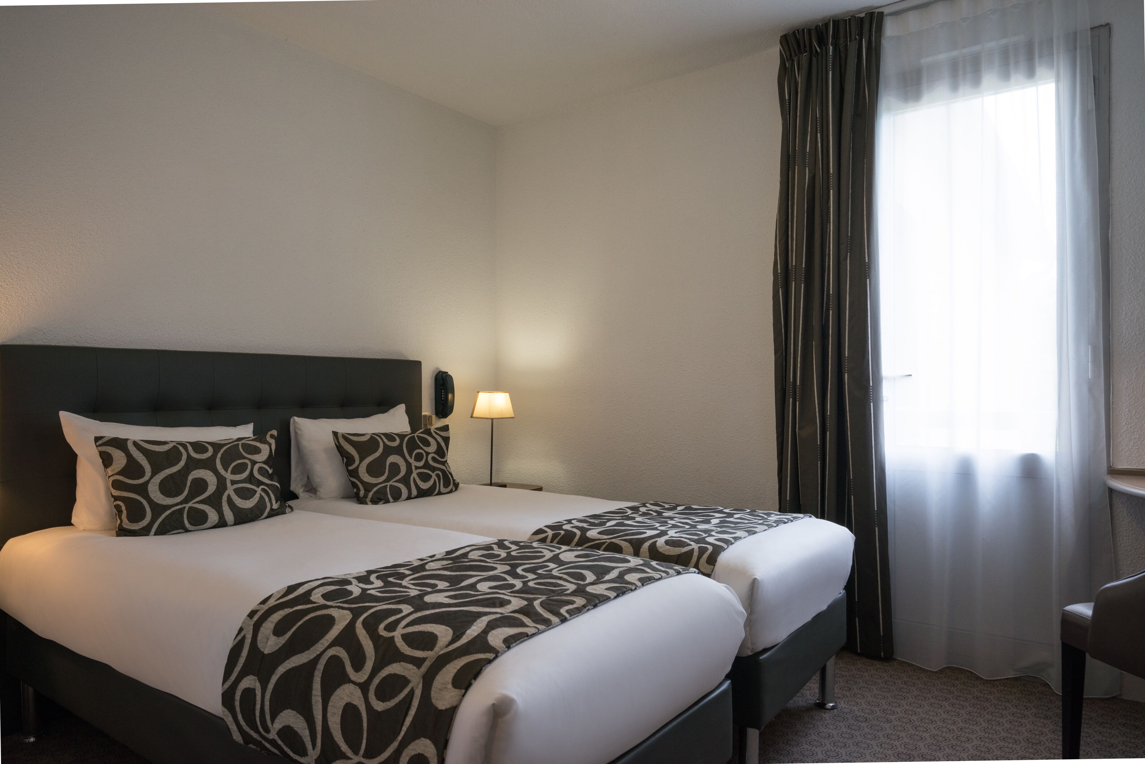 A hotel room with two beds, a desk, and a chair.