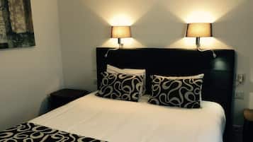 Una cama bien hecha con ropa de cama estampada, dos lámparas de noche y un cabecero oscuro.