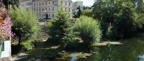 Un hotel de estilo arquitectónico europeo clásico, con un camino pavimentado y una masa de agua que refleja la vegetación circundante.