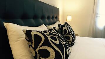 A bed with a dark headboard, white and patterned pillows, and a bedside lamp.