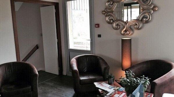 A room with two leather chairs, a table with magazines and a plant, a tall floor lamp, and a decorative mirror on the wall. - Hôtel du Moulin, Niort (Niort)