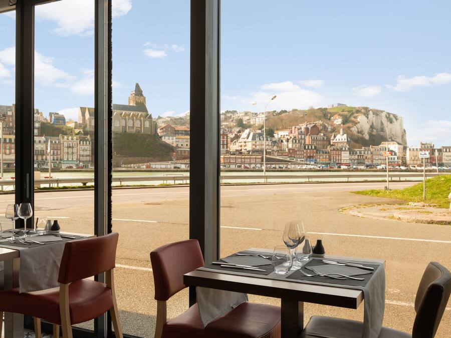 A restaurant with tables set for dining, featuring a view of a historic town and a prominent hill in the background.