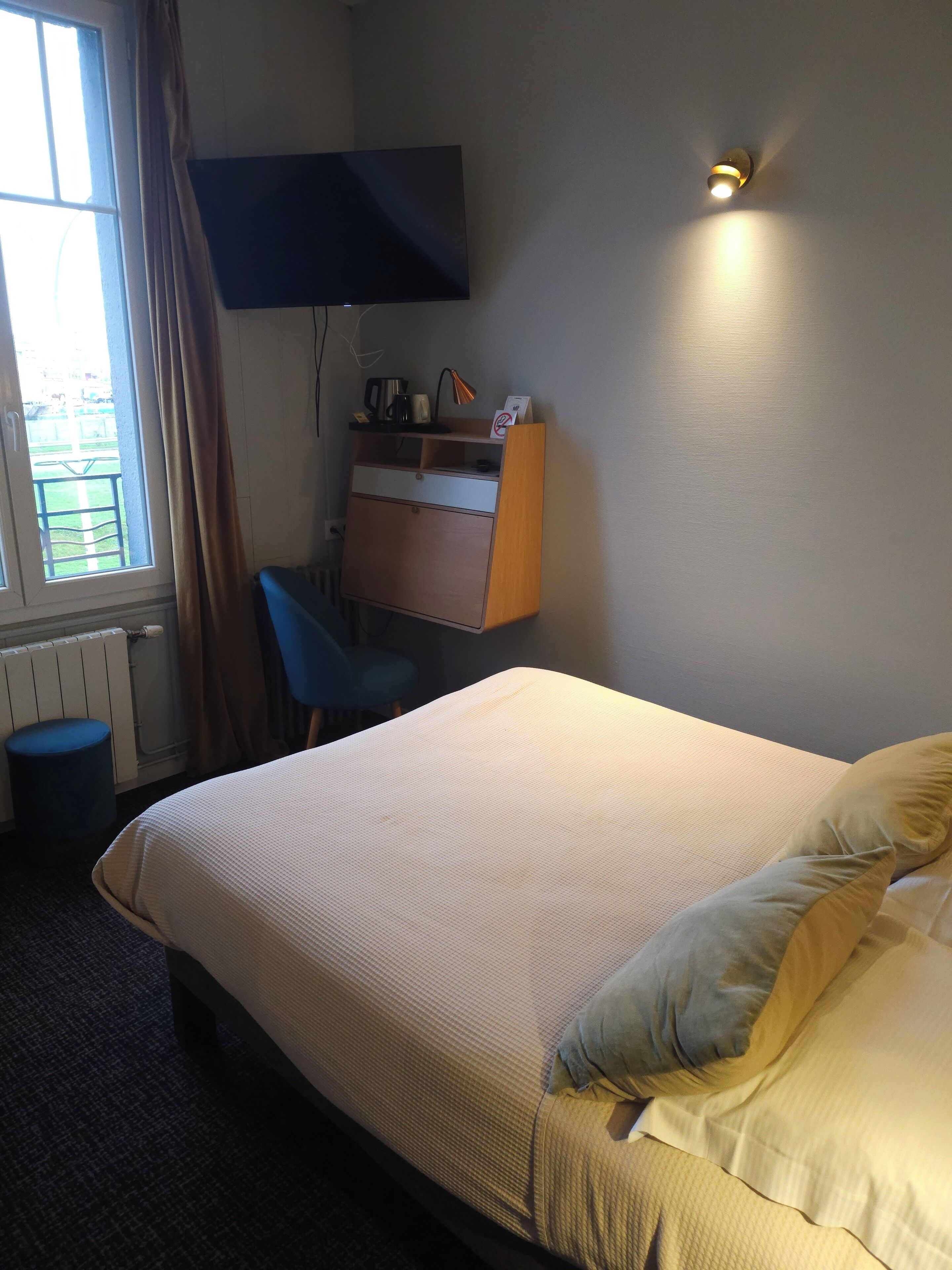 A hotel room with a bed, a desk, a chair, a television, and a window with curtains.