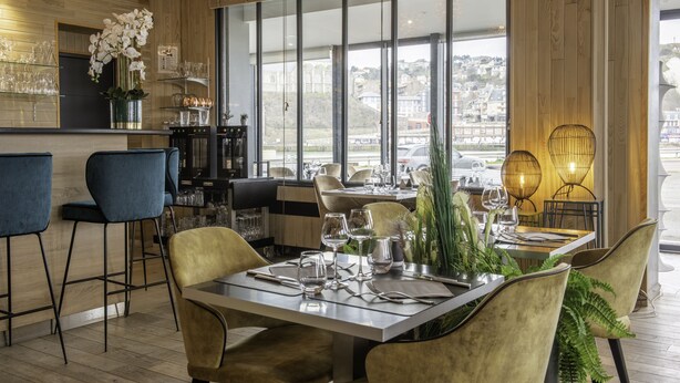 Ein Restaurant mit Barbereich, Holzpaneelen, großen Fenstern und Blick auf die Stadt.