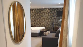 A hotel room with a large round mirror, a bed, a sofa, and a patterned wallpaper.