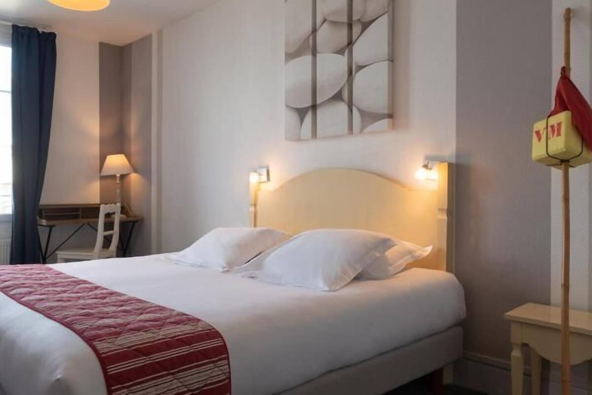 Une chambre d’hôtel avec un lit, un bureau, une chaise et une fenêtre avec des rideaux.