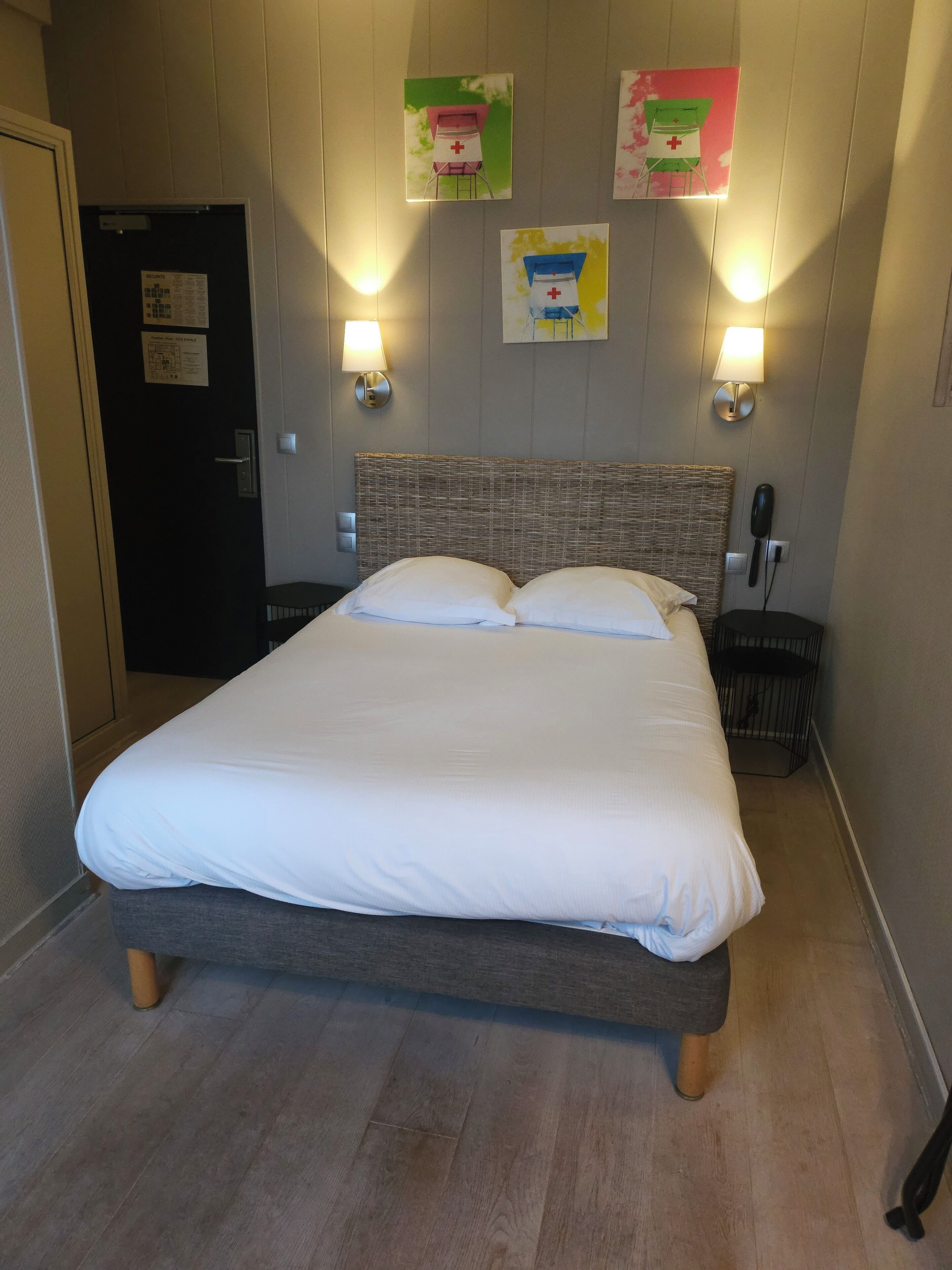 A hotel room with a large bed, two bedside lamps, a telephone, and a door with a sign.