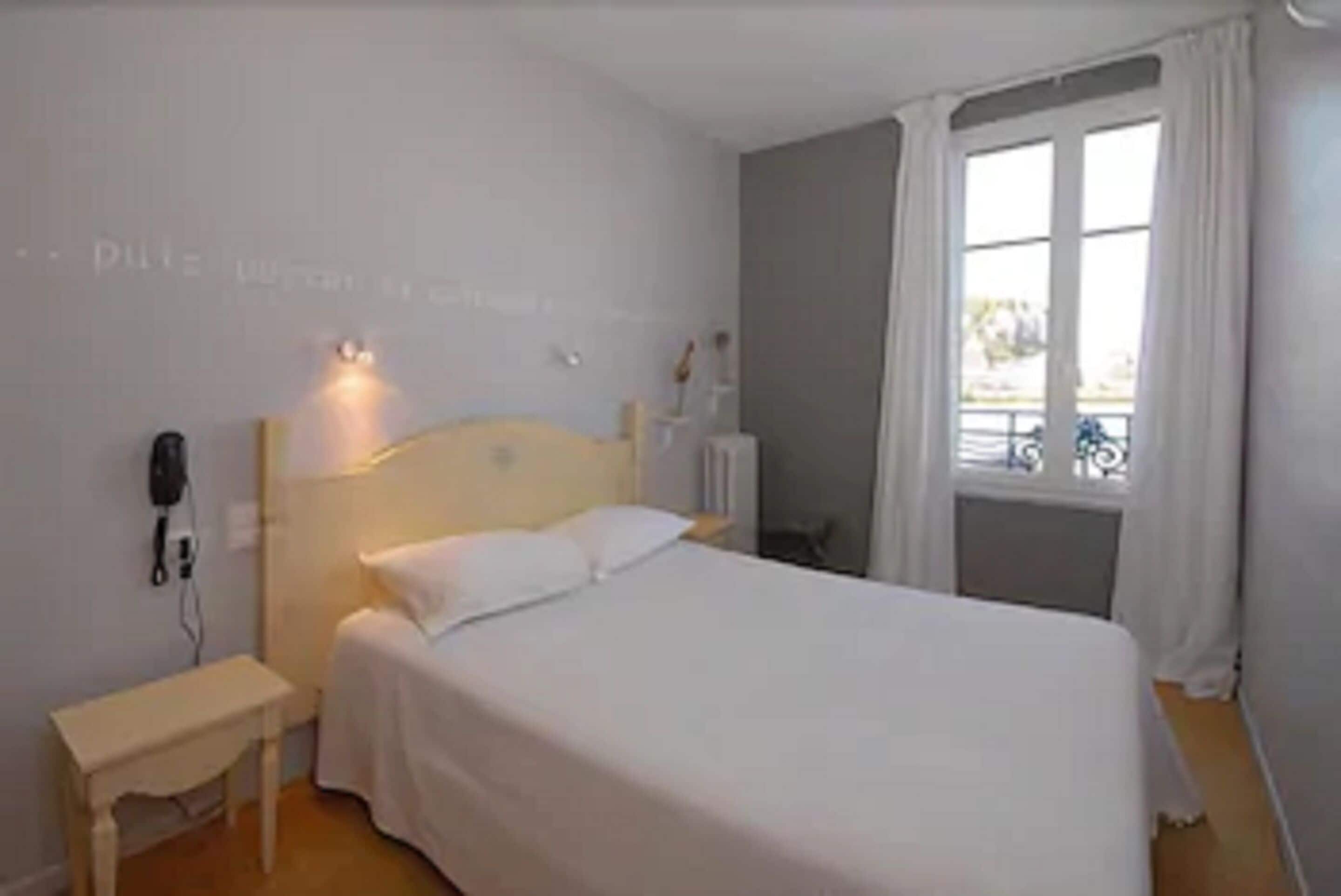 A bedroom with a single bed, a bedside table, a lamp, and a window with curtains.