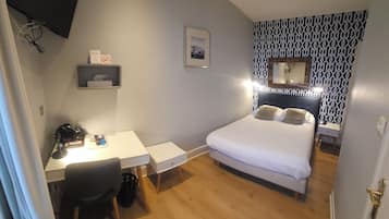 Un dormitorio con cama, escritorio y silla. Hay un estante pequeño con un cuadro enmarcado y un espejo sobre la cama.