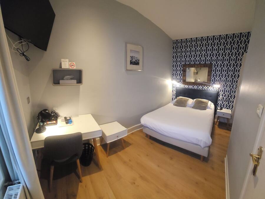 Un dormitorio con cama, escritorio y silla. Hay un estante pequeño con un cuadro enmarcado y un espejo sobre la cama.