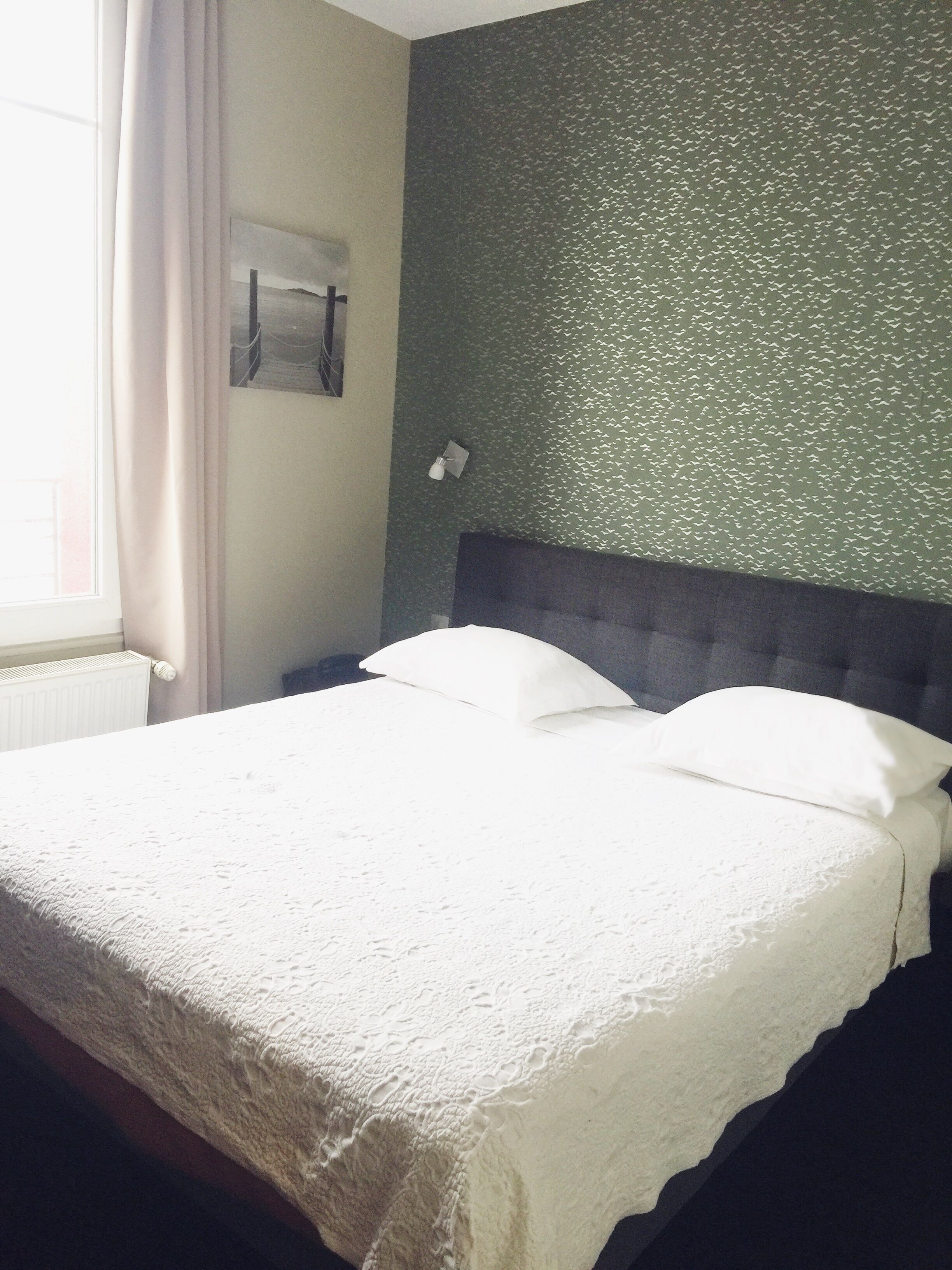 Een netjes opgemaakt bed met een witte deken en kussens, een grijs hoofdbord en een groen gestructureerde muur.
