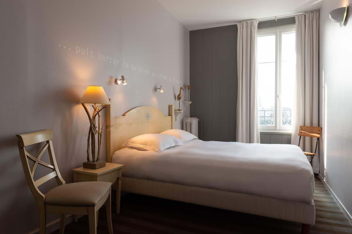 Un lit bien fait dans une chambre d’hôtel, avec vue sur la ville par la fenêtre.