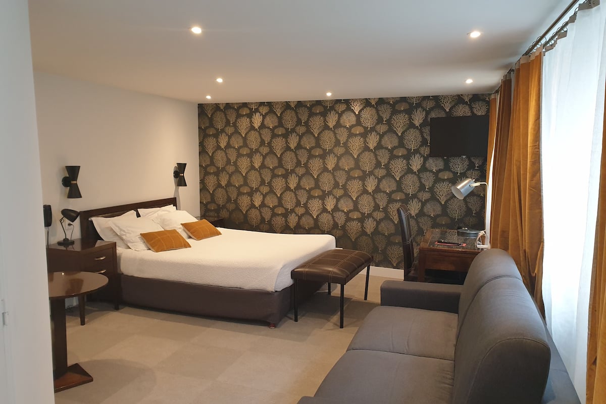 Une chambre d’hôtel avec un lit, un canapé, une petite table et un téléviseur fixé au mur.