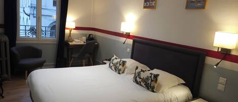 A hotel room with a large bed, a desk, a chair, and a window with curtains.