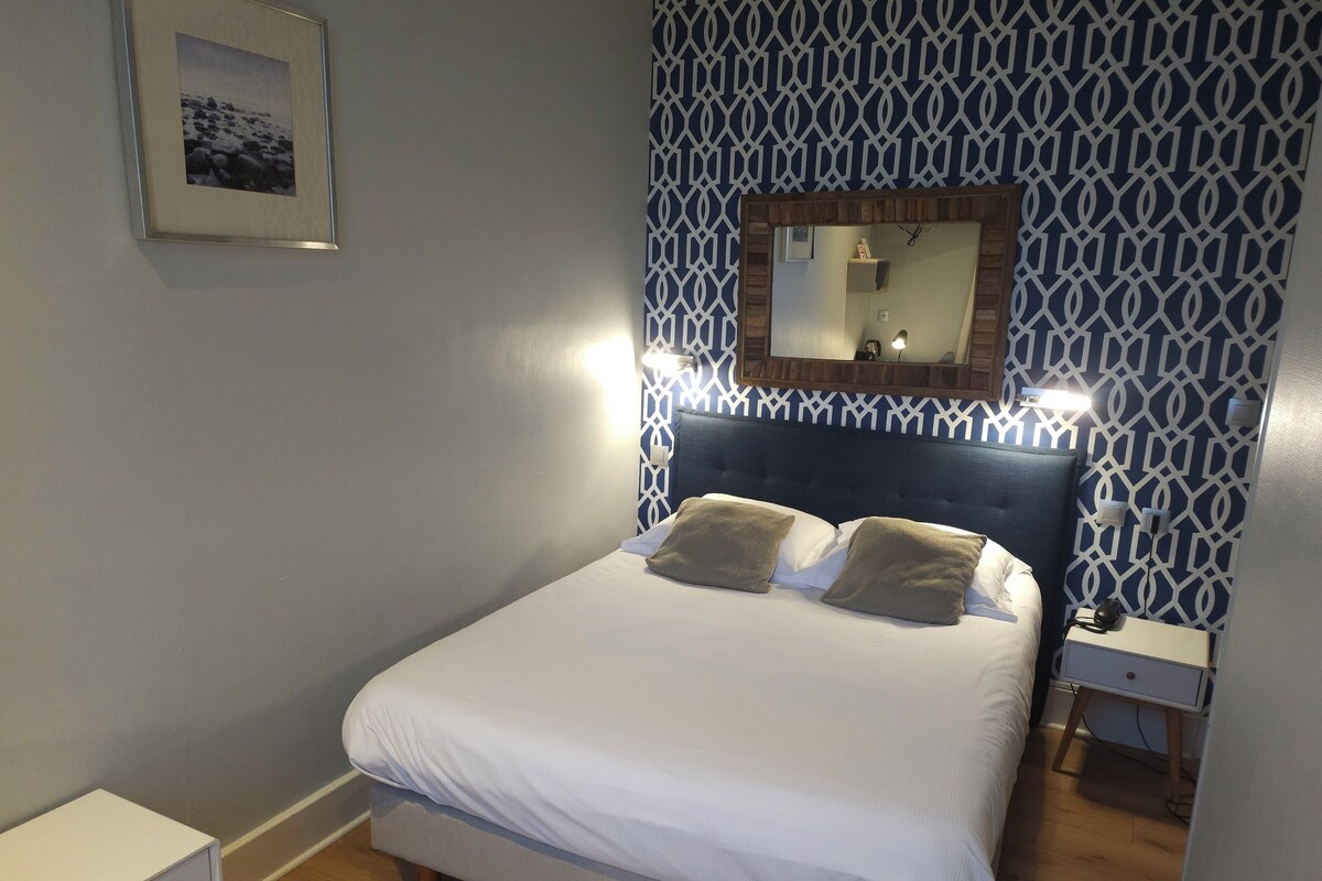 Een net opgemaakt bed met twee kussens, een nachtkastje en een spiegel erboven.